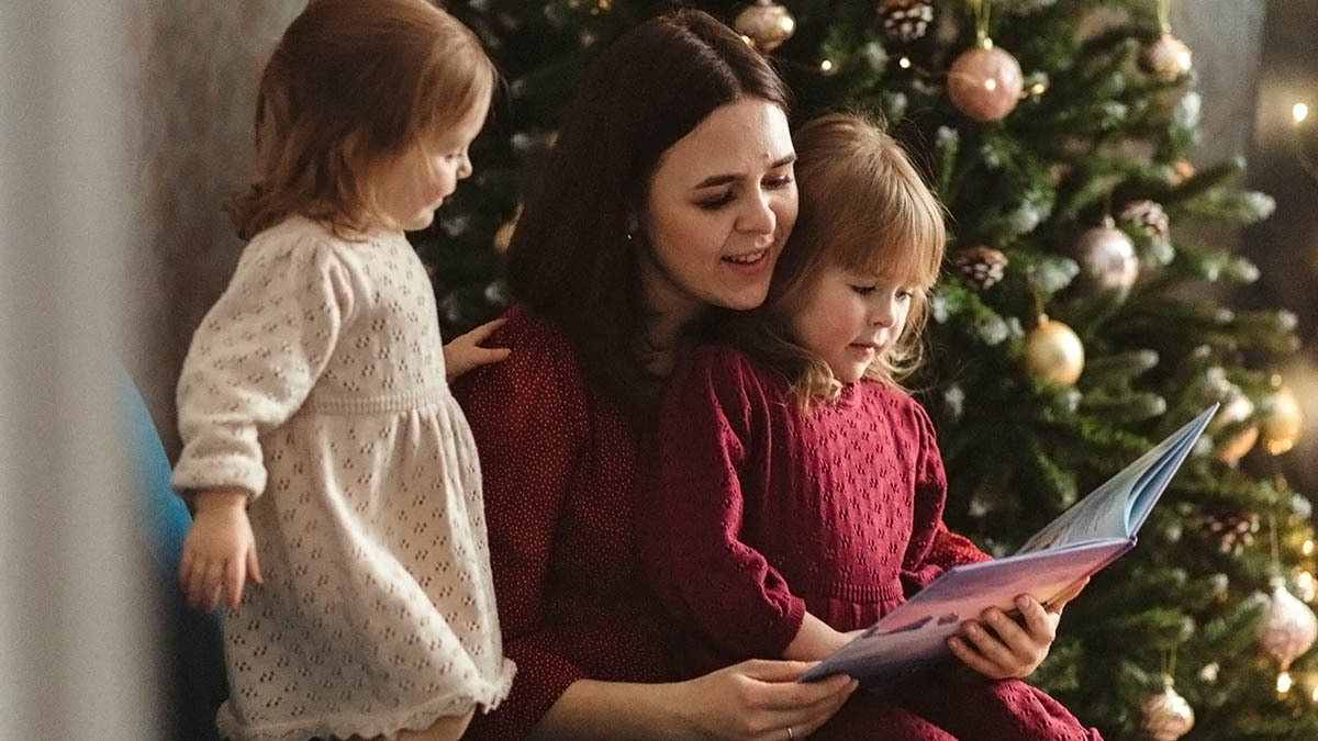 A mother reads the Bible to her children by their Christmas tree