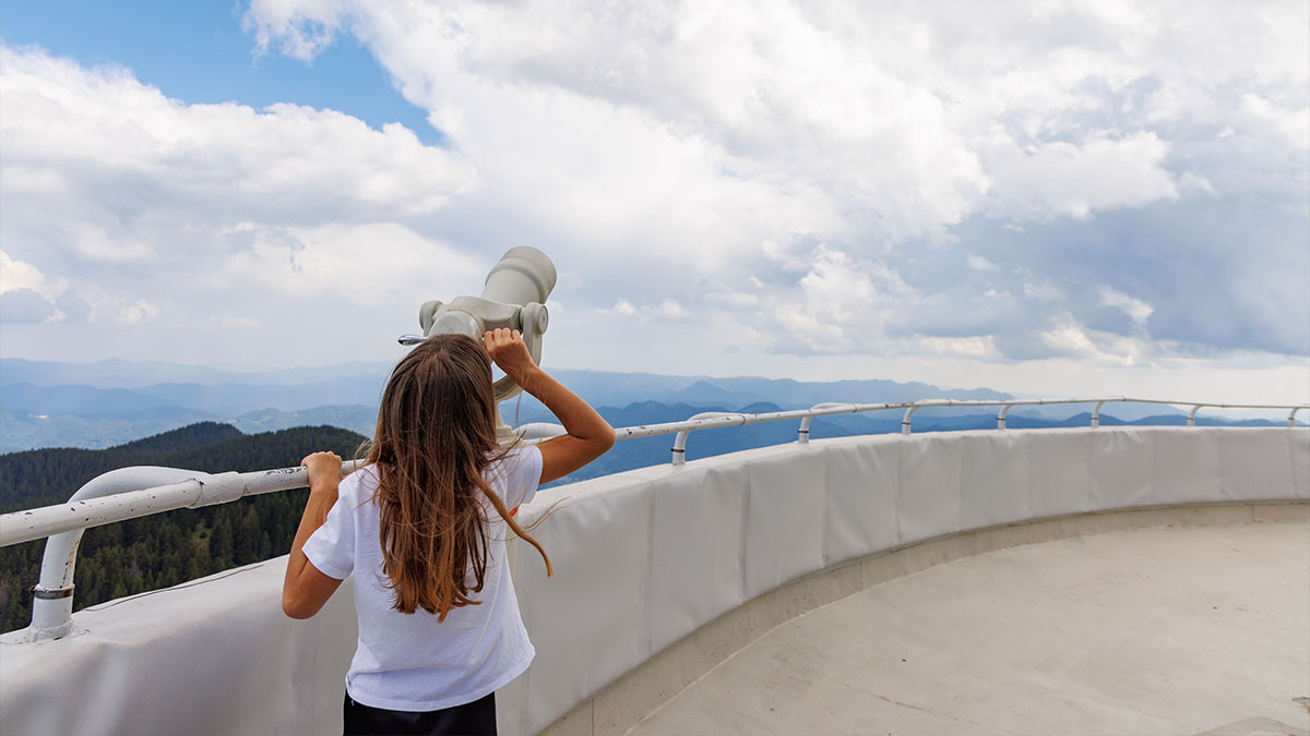 A girl looks at the sky through lookout binoculars