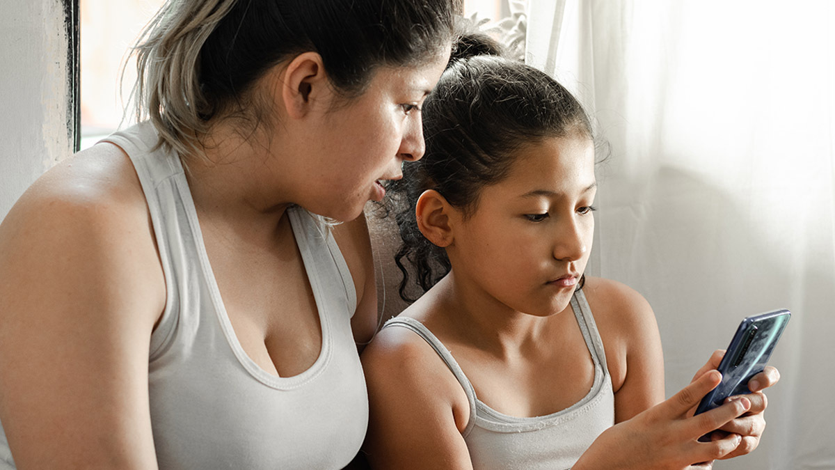 A little girl and her mother look at a phone together