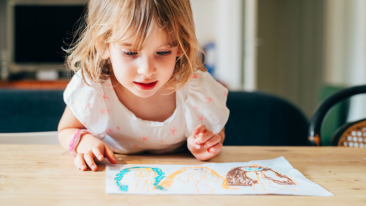 A young girl looks at a drawing she made of three people