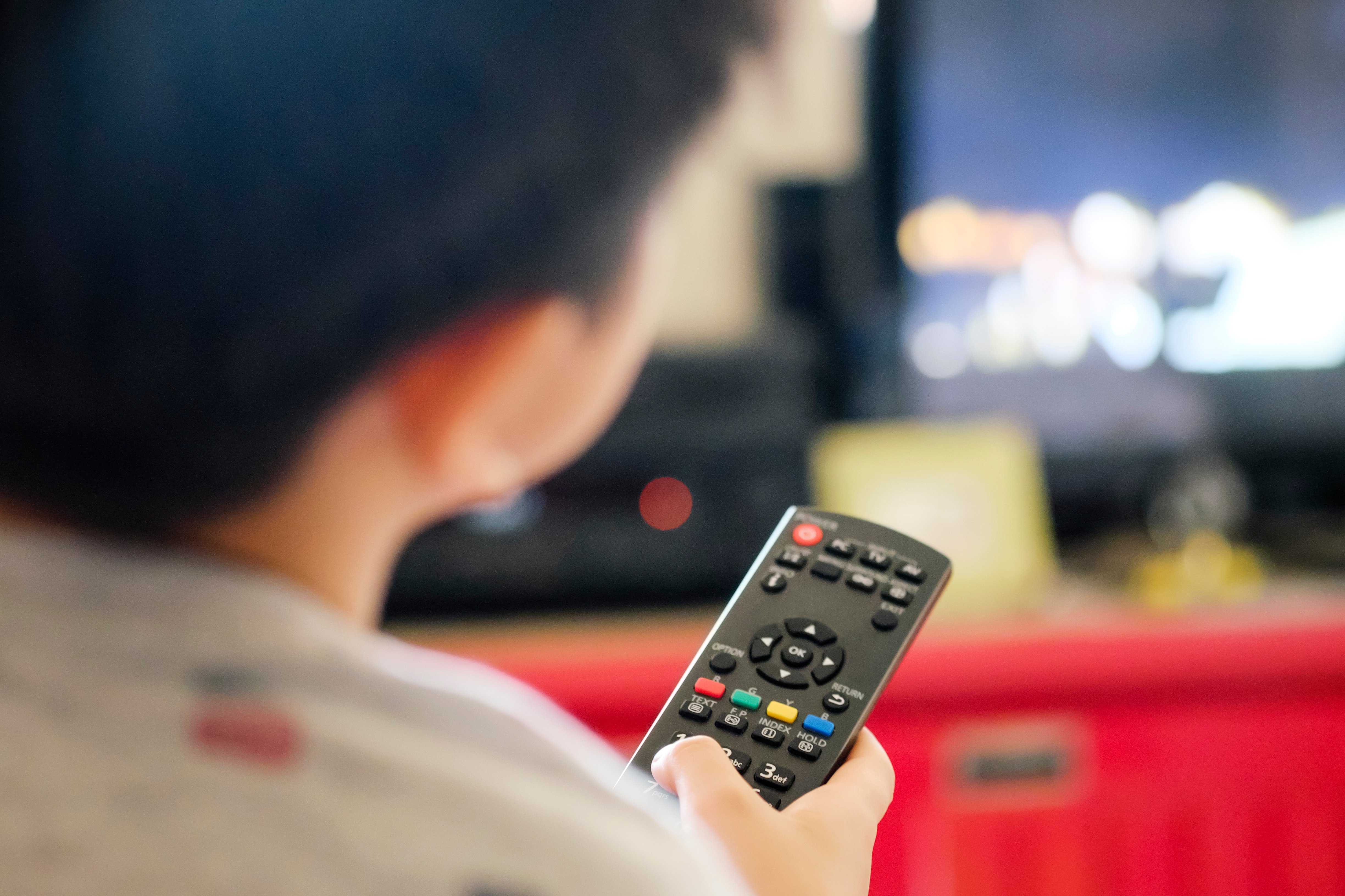 A young boy holds a tv remote and watches the tv