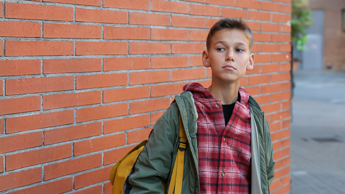 A boy standing by a brick wall