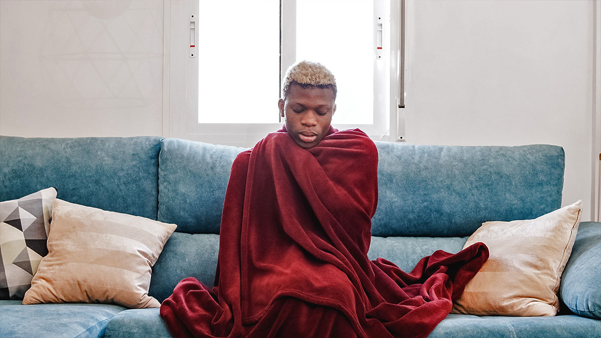 A transgender person sits on a couch and covers their body with a blanket
