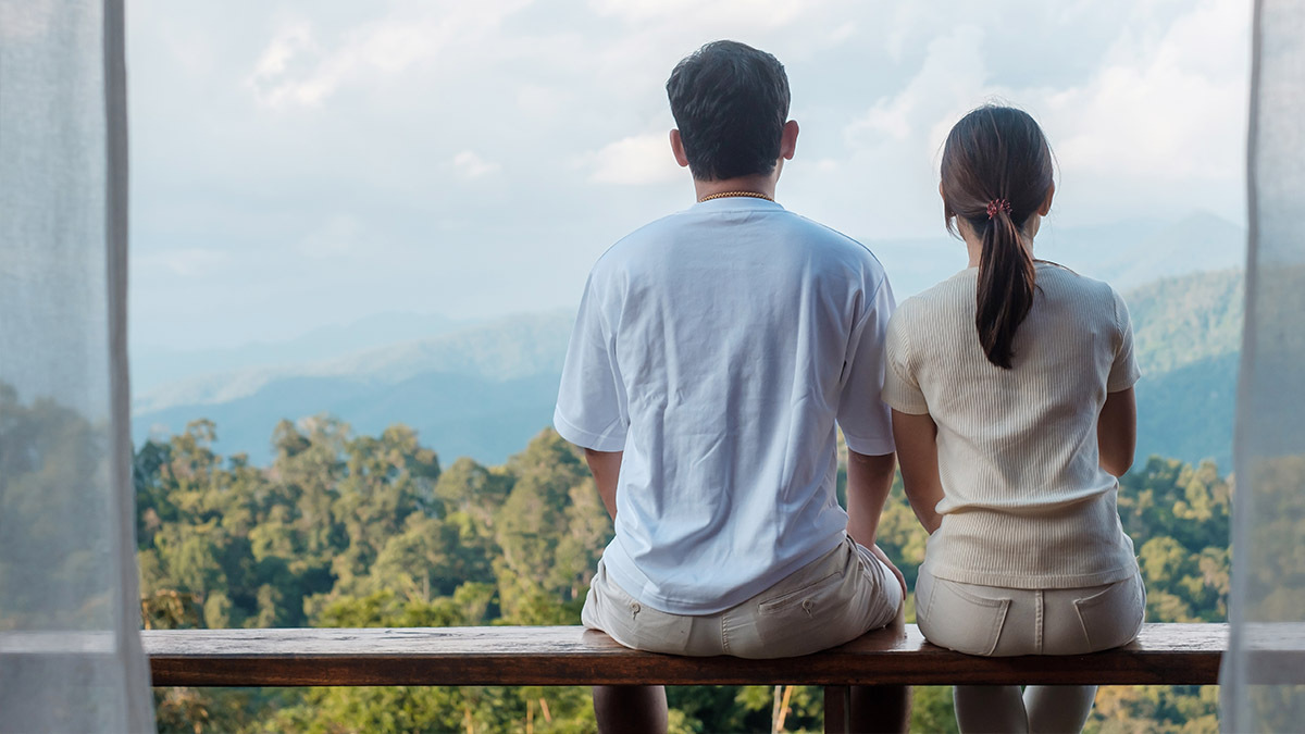 A man and woman sit on a railing and look out onto some scenery