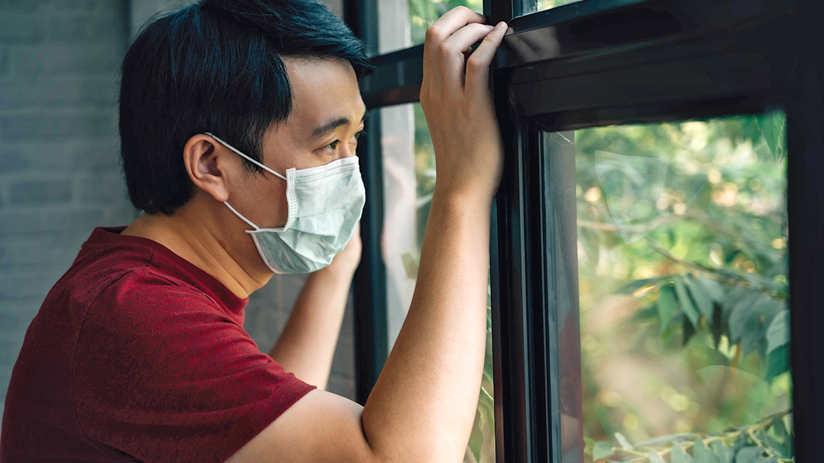 A man wearing a medical mask looks longingly out of the window