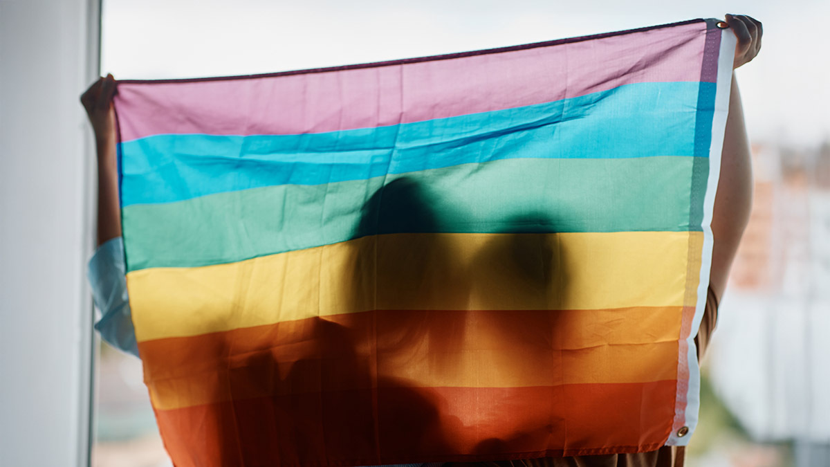The silhouettes of two women can be seen through a gay pride flag