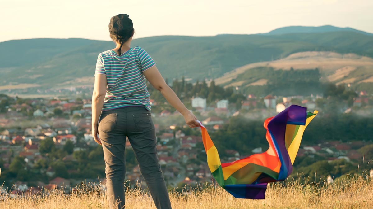 A woman holds a gay pride flag on a hill that overlooks a city
