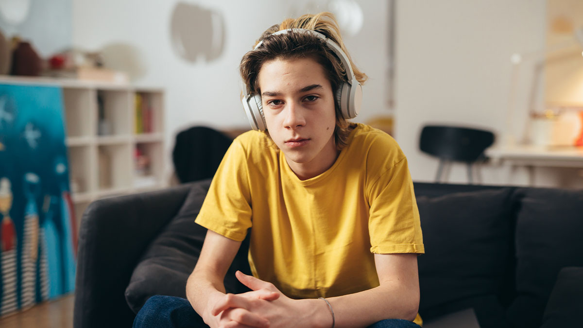 A teen boy wears headphones and looks seriously at the camera
