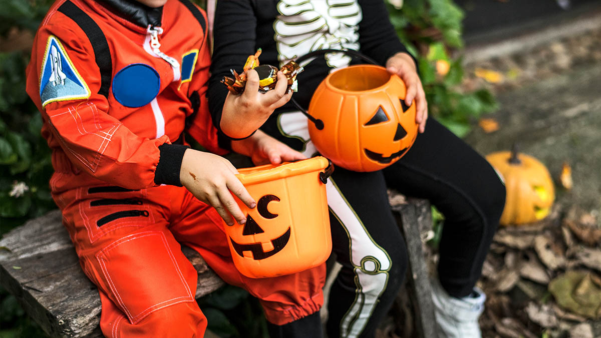 Two young boys in halloween costumes hold candy and trick or treat buckets