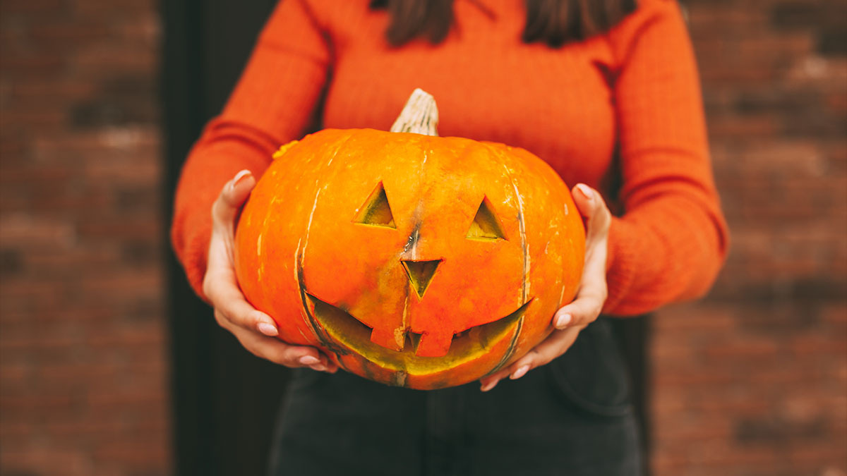 A woman holds a large jack o’lantern in her hands