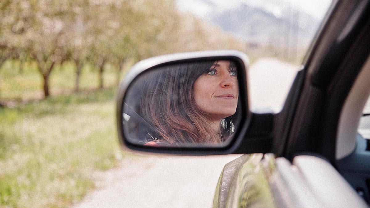 A woman's reflection can be seen in a car side mirror