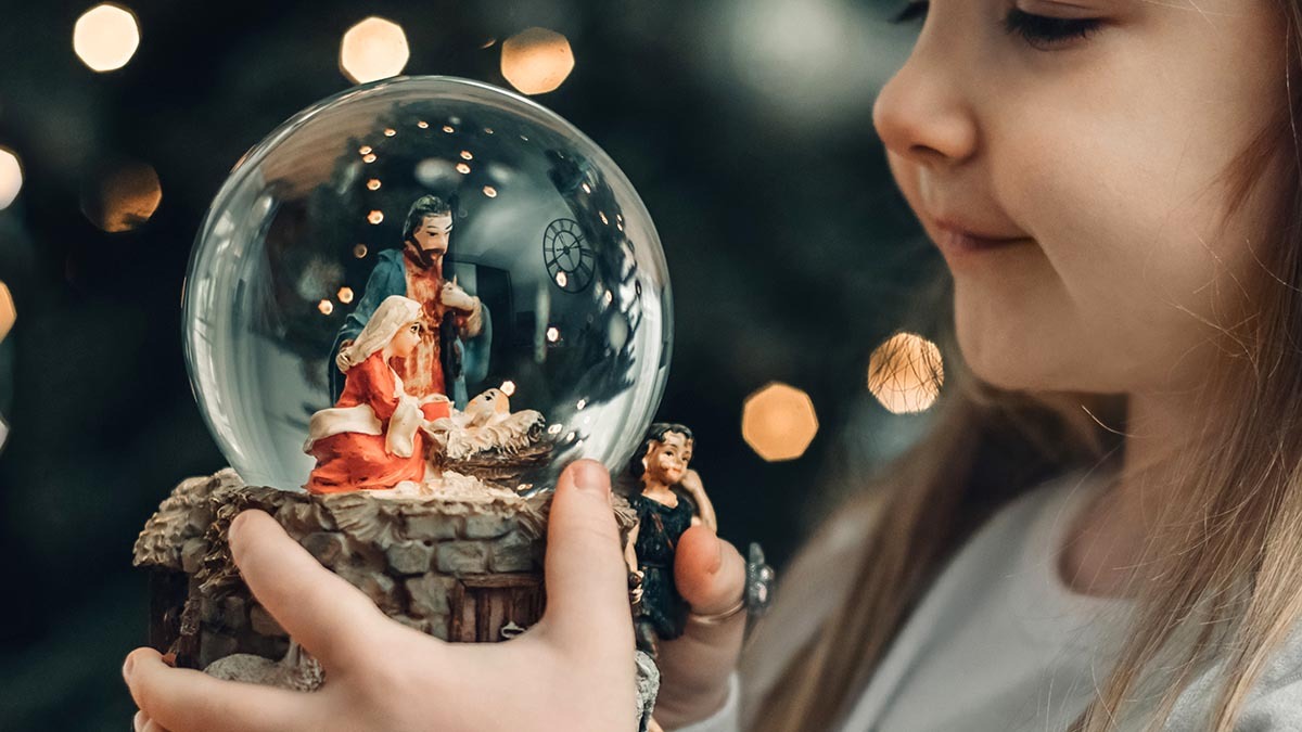 A young girl gazes at a nativity snow globe that she holds in her hands