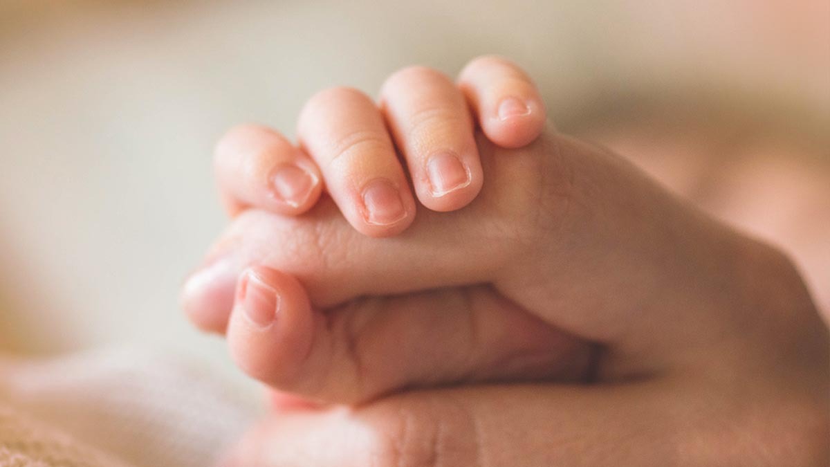A baby holds onto his parent's finger