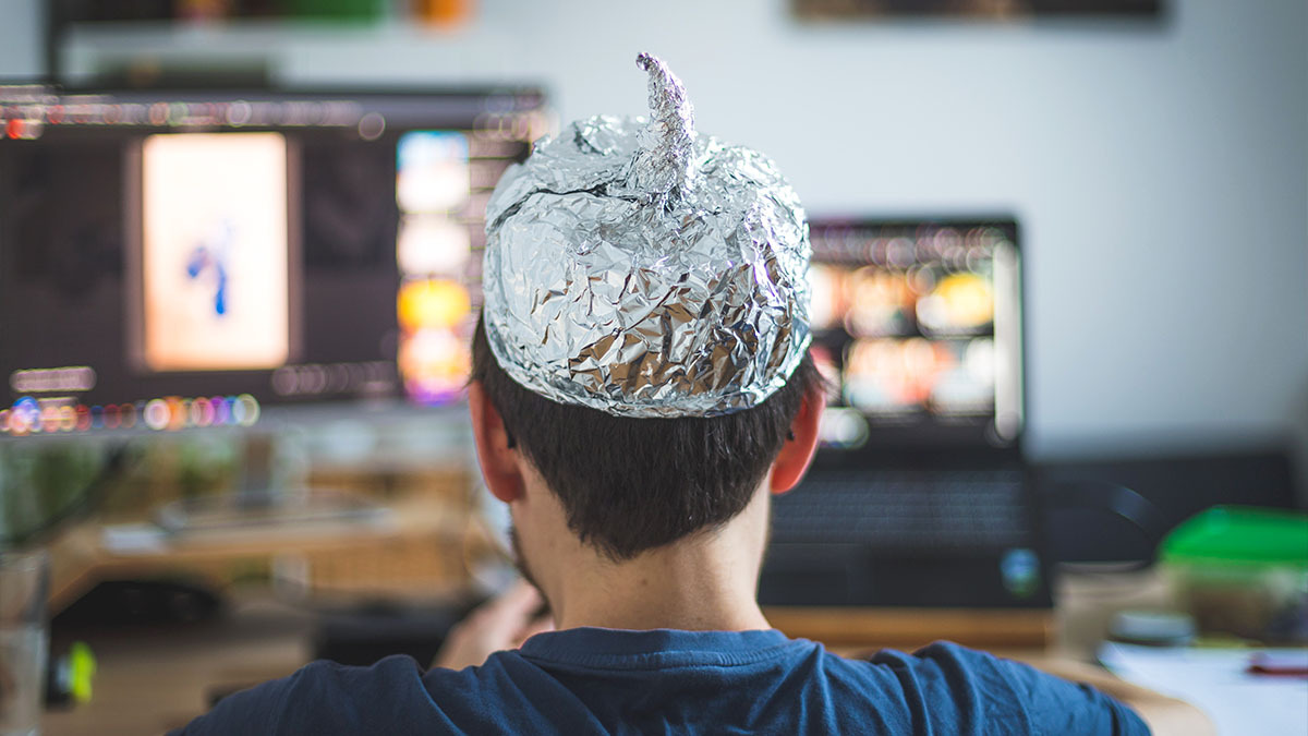 A man wearing a tin foil hat looks at his computer screens