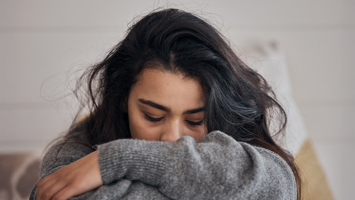 A tired young woman buries her face in her arms