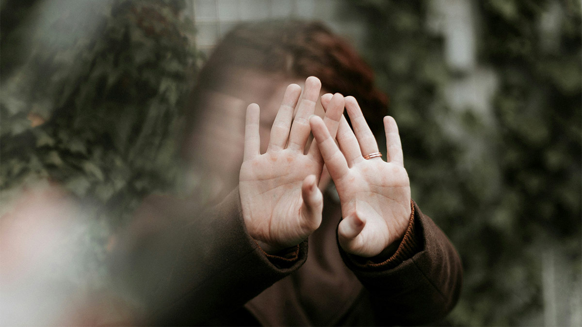 A scared woman holds her hands in front of her face