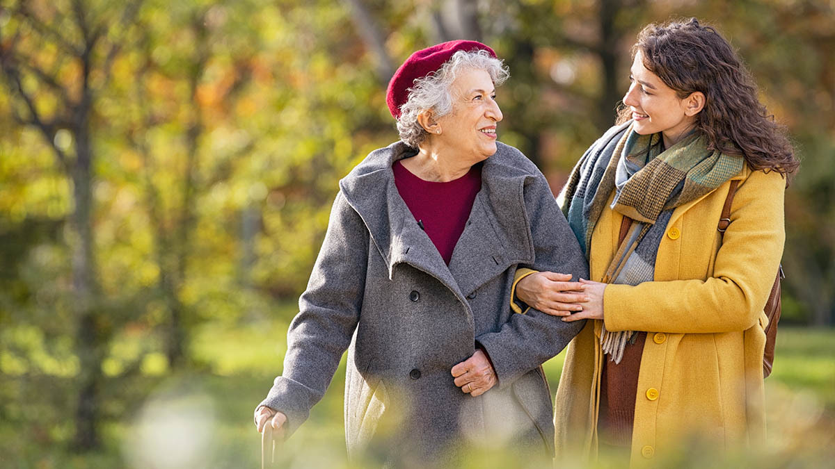 A young woman helps an elderly woman walk through the park