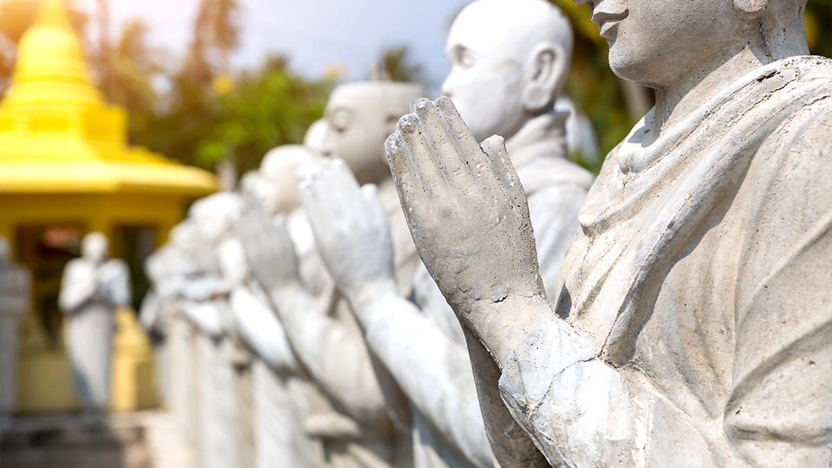 A line of people statues in a Buddhist temple fold their hands as if in prayer