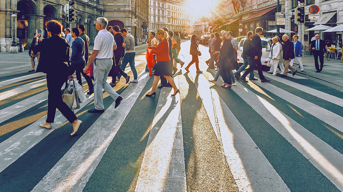 Many people walk on a crosswalk in a busy city