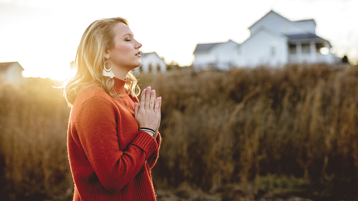 A woman prays outdoors beside her house