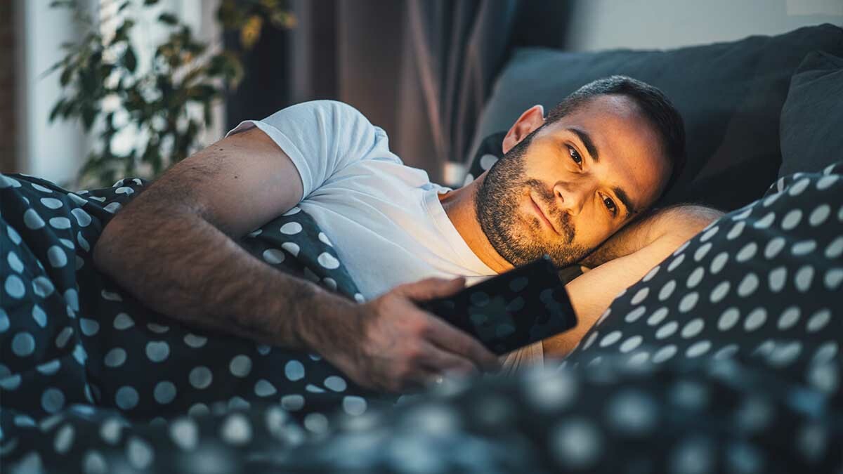 A man lies in bed staring at his phone