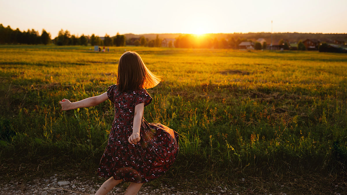 A young girl dances in a field at sunset