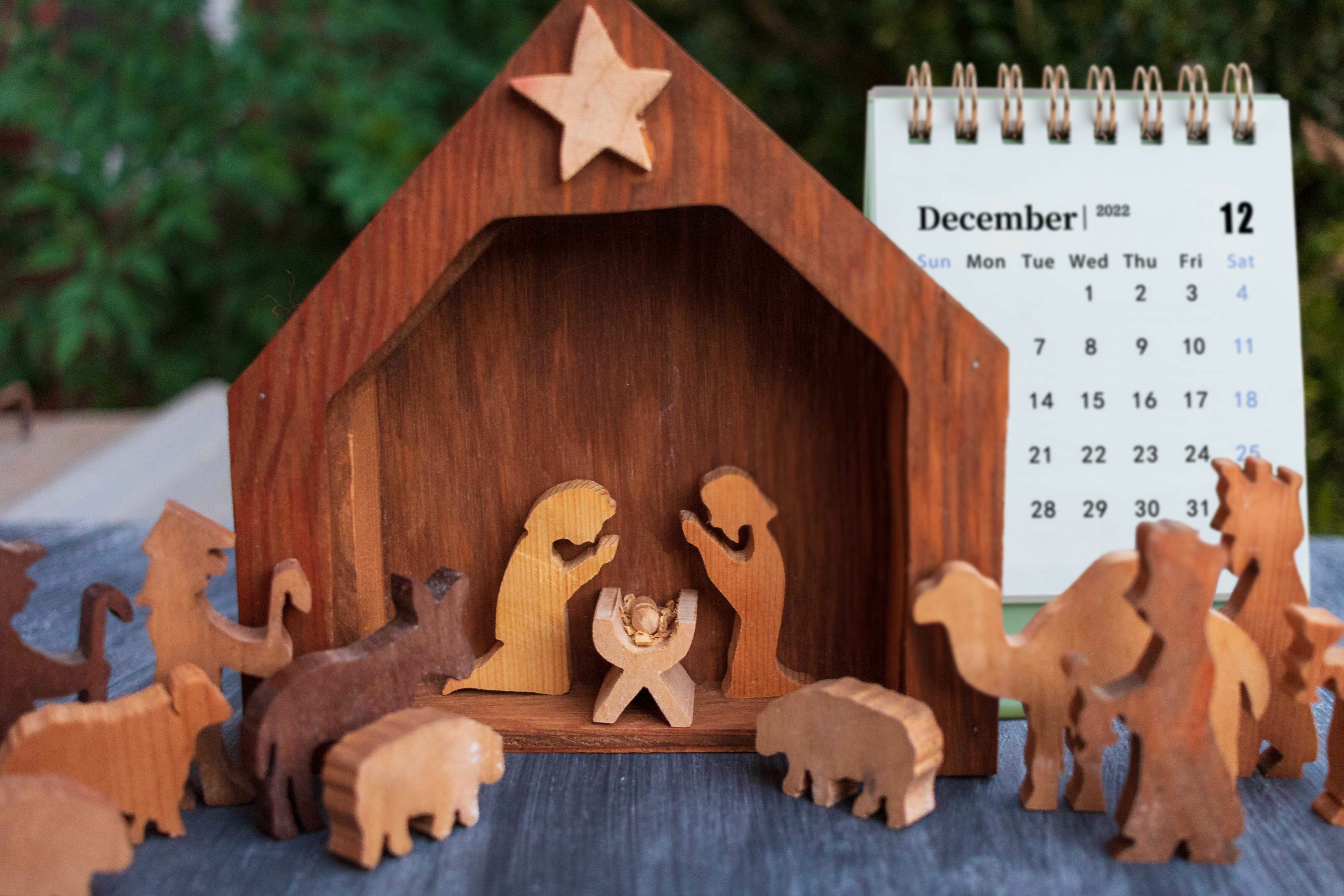 A nativity scene in front of a Christmas tree and calendar