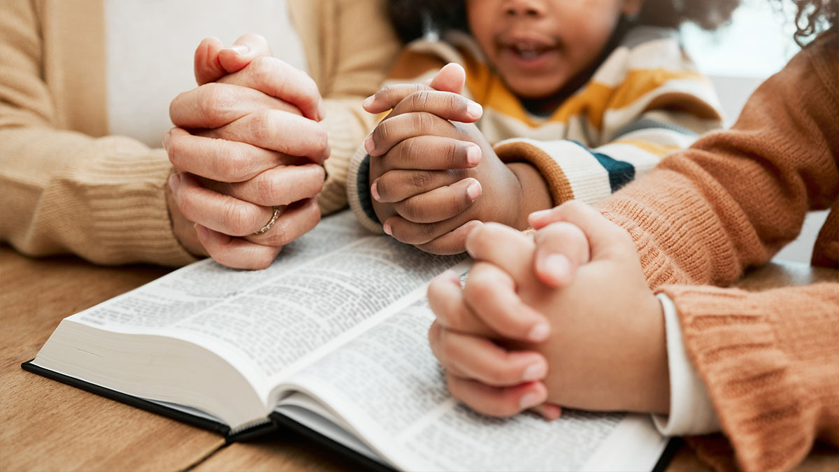 Two children pray with their mother as they read the Bible together as a family