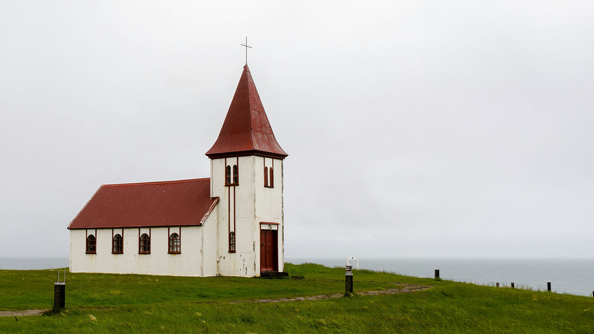 A church with a steeple stands alone against a cloudy sky