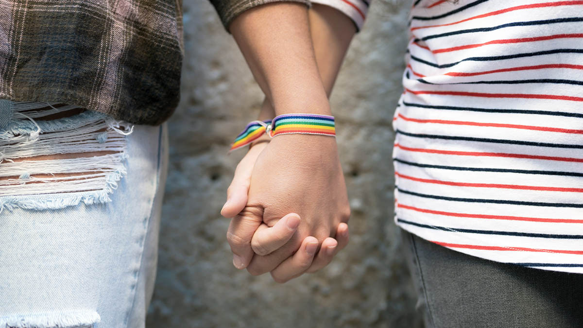 A gay couple holding hands, each wearing a gay pride bracelet