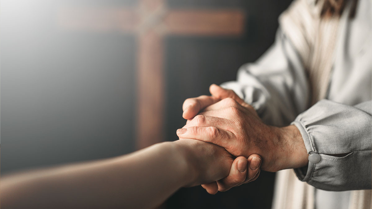 Jesus clasps a person’s hands in his as they stand in front of a cross