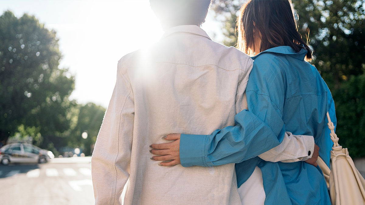 A young couple walk down the street with their arms around each other