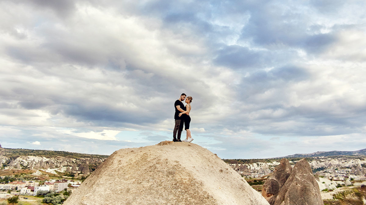 A heterosexual couple stands on top of a mountain overlooking a town