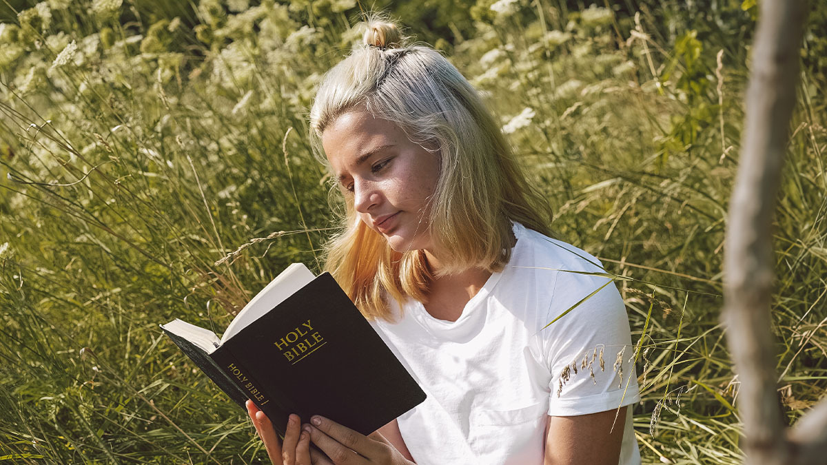 A teen girl reading a Bible outdoors