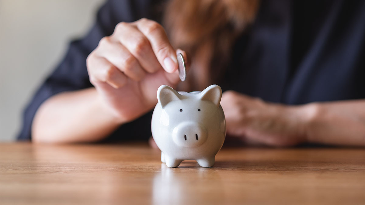 A woman puts a coin inside of a piggy bank