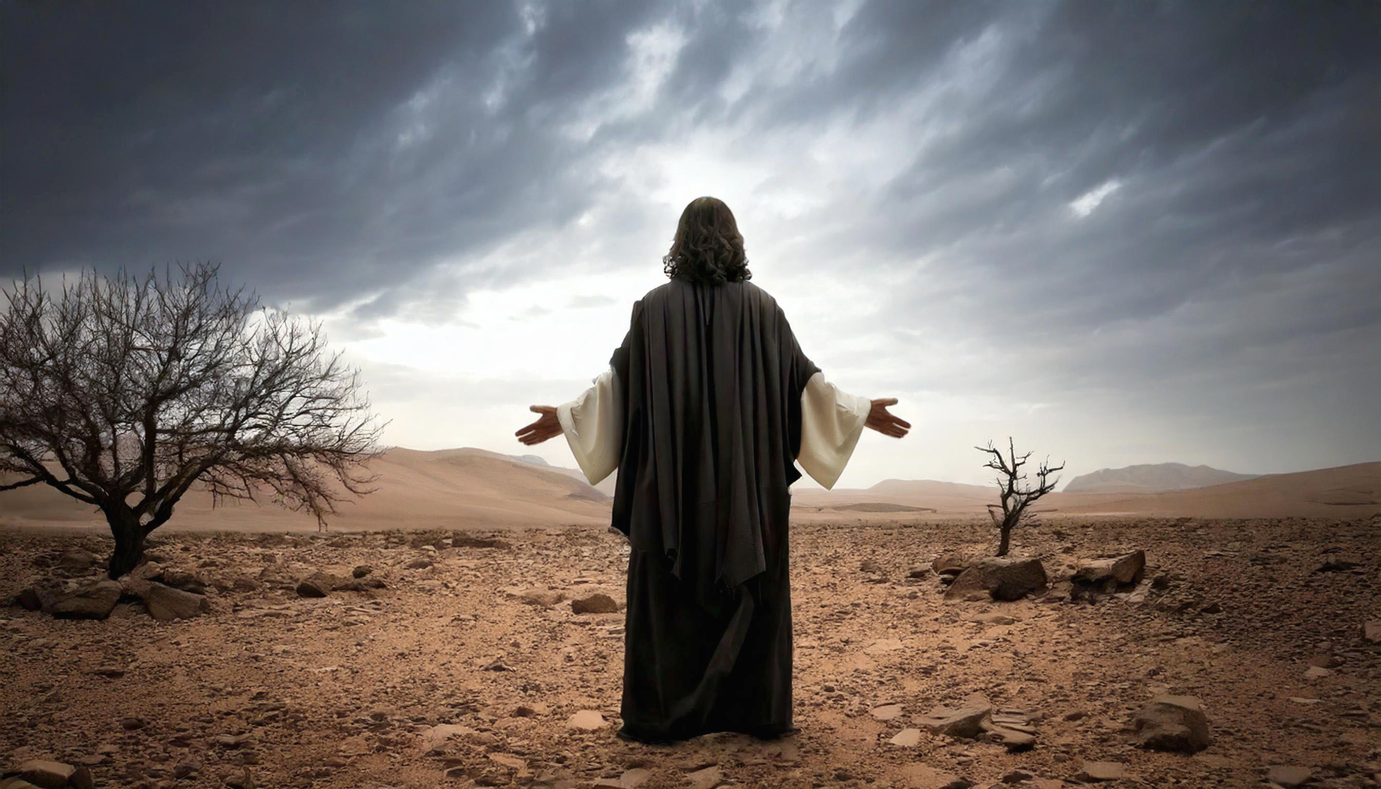 Jesus Christ looks to the sky with his hands outspread while he stands in a desert wilderness