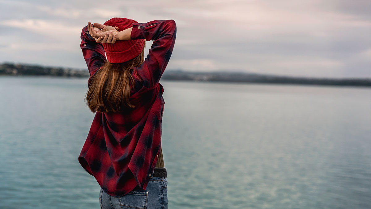 A young single woman looks out over a lake