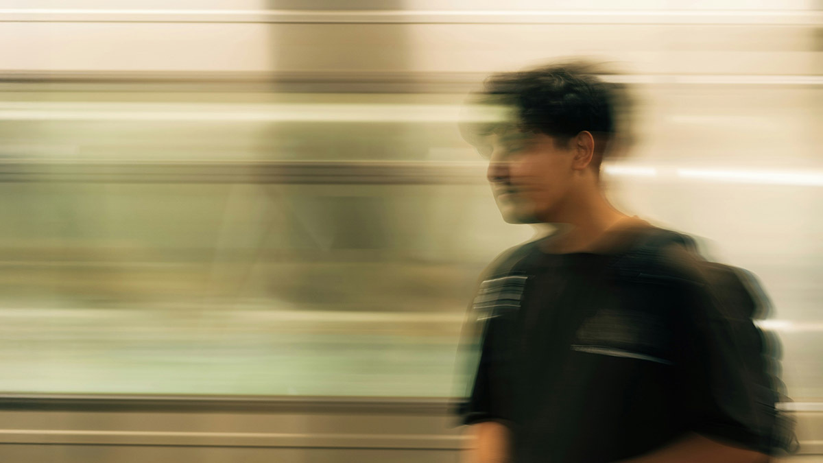 A young man stands on a subway platform and looks blurred as the train goes by