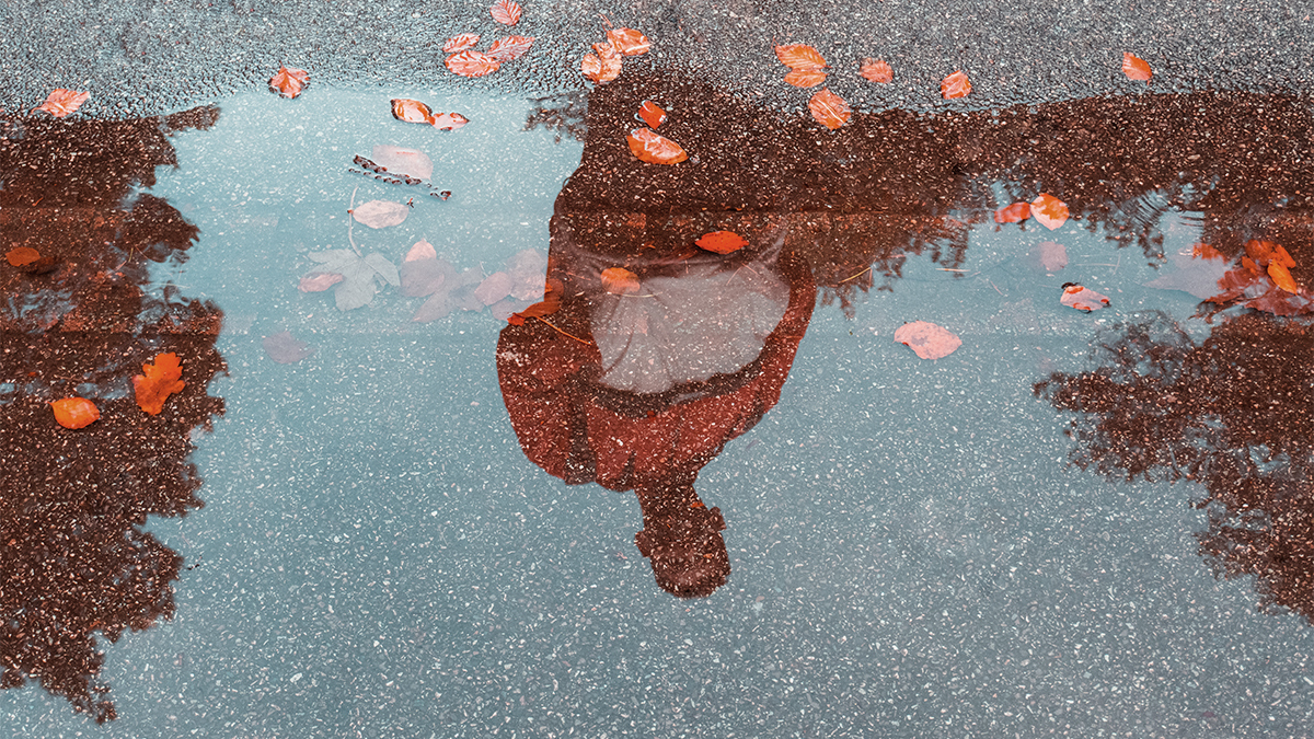 A young man looks at an obscured reflection of himself in a puddle
