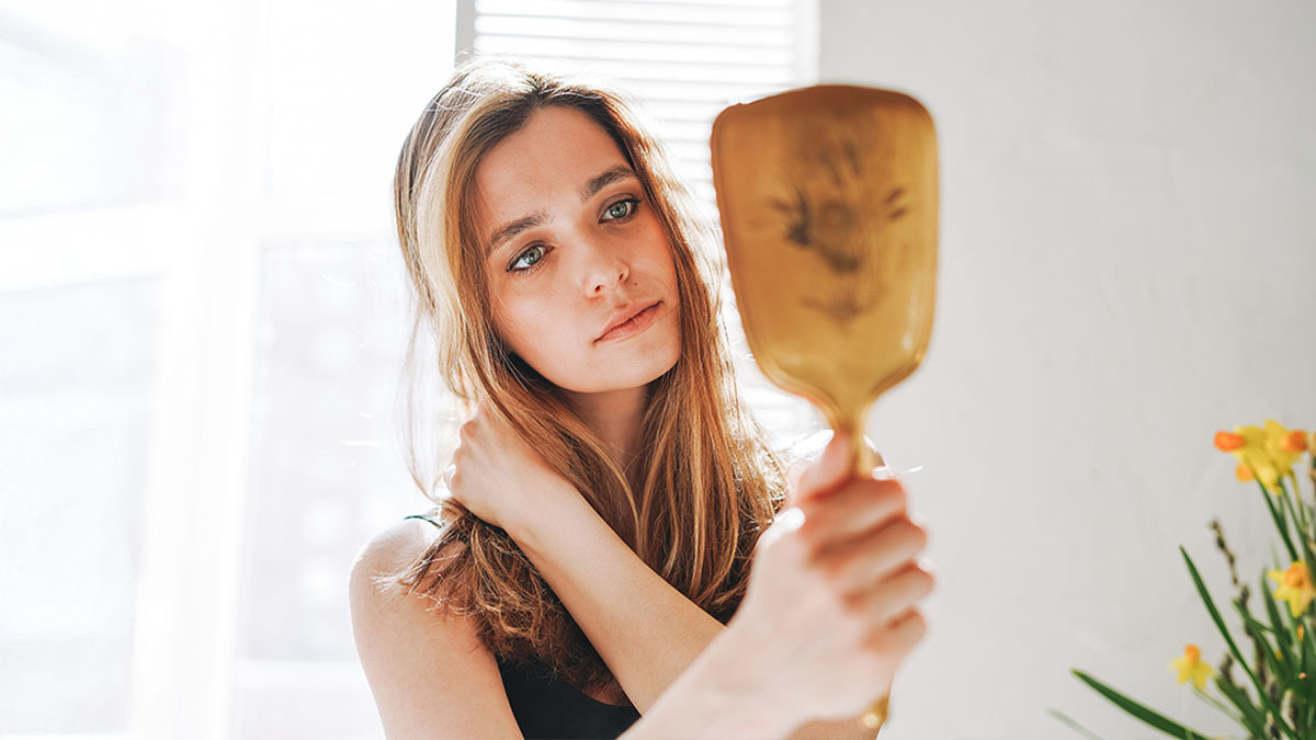 A young woman looks at her reflection in a handheld mirror