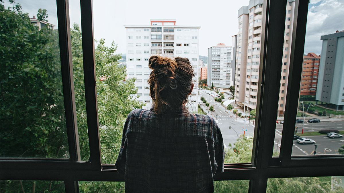 An anxious girl looks out an apartment window at the city