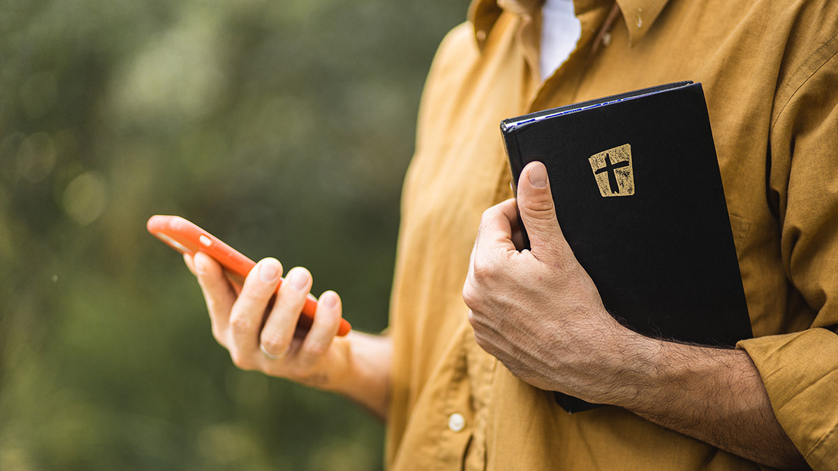 A man holds his Bible while scrolling on his phone
